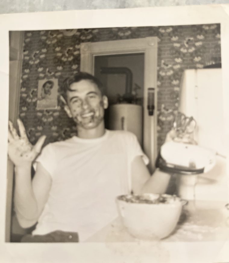 Poppa in the kitchen in the 1950s, grinning with batter on his face and hand beside a big mixing bowl